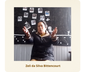 Mulher branca, de cabelos curtos e grisalhos. Usa uma blusa na cor marrom clara sobreposta por um casaco preto de ziper fechado.